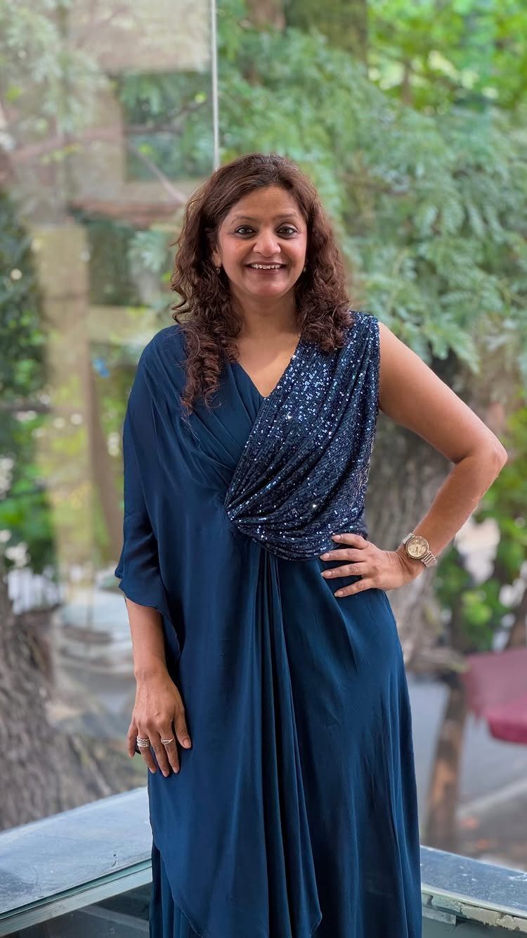 Woman wearing a navy blue sequined gown posing outdoors with green trees behind.