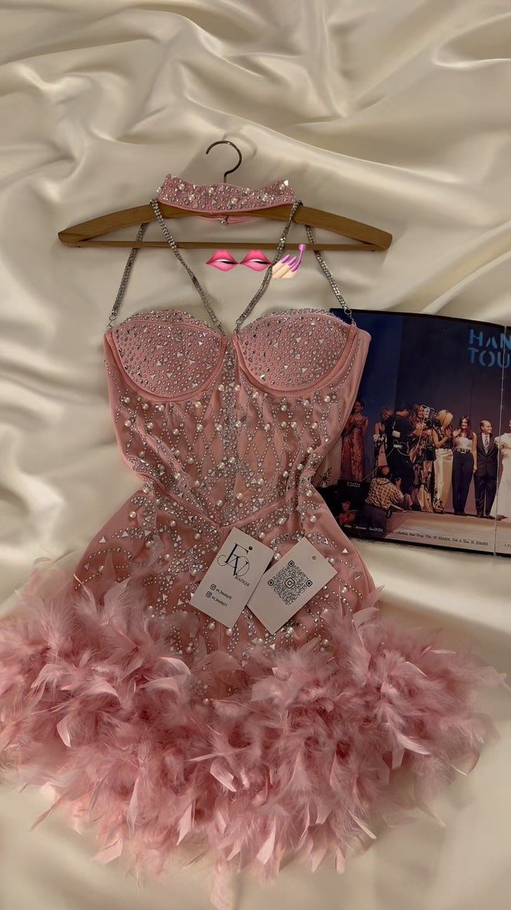 Pink rhinestone corset mini dress with feather skirt hanging on a wooden hanger