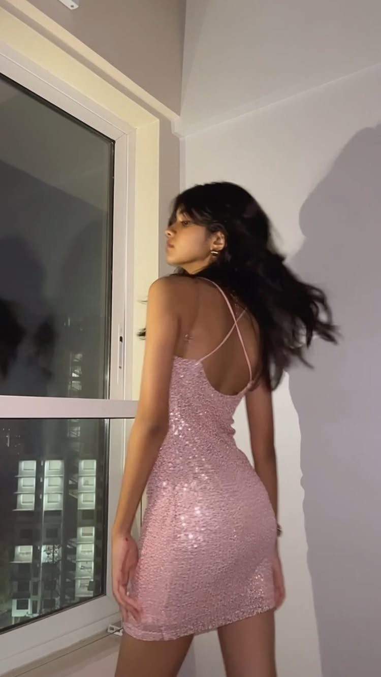 Woman wearing a pink sequin mini dress standing by a window at night