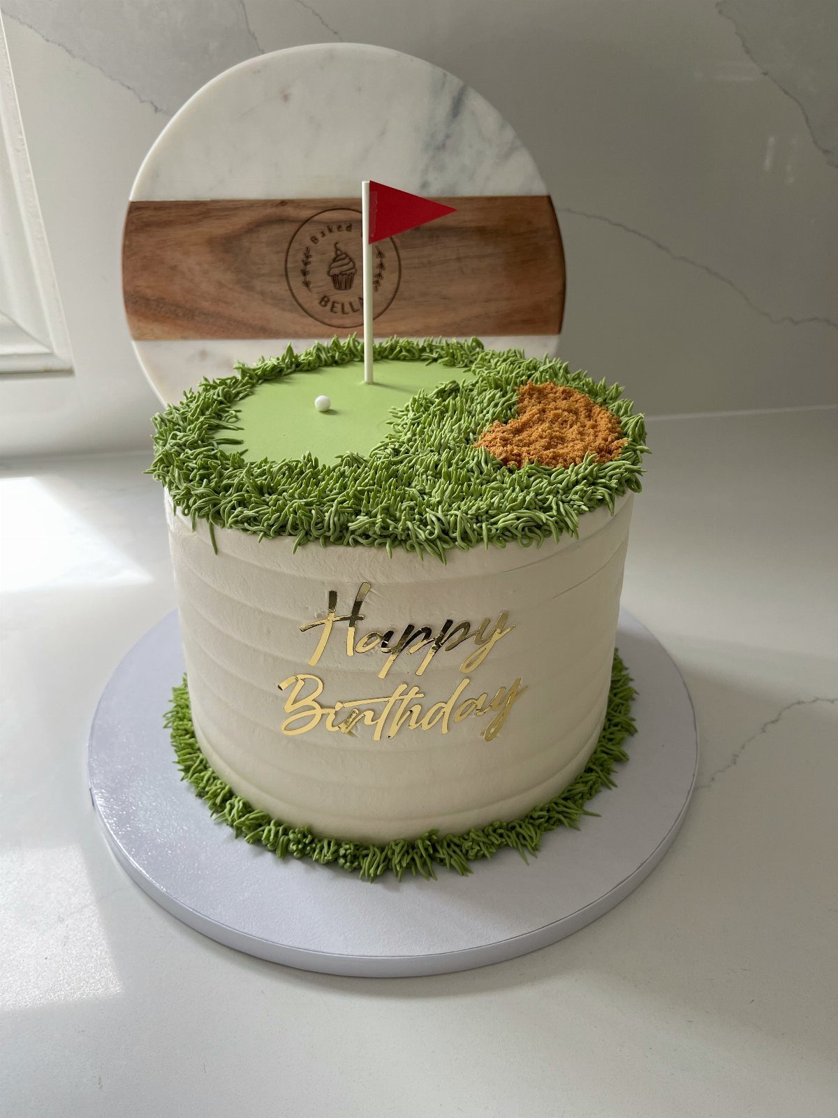 Golf themed birthday cake with green grass frosting, a red flag, and gold lettering.