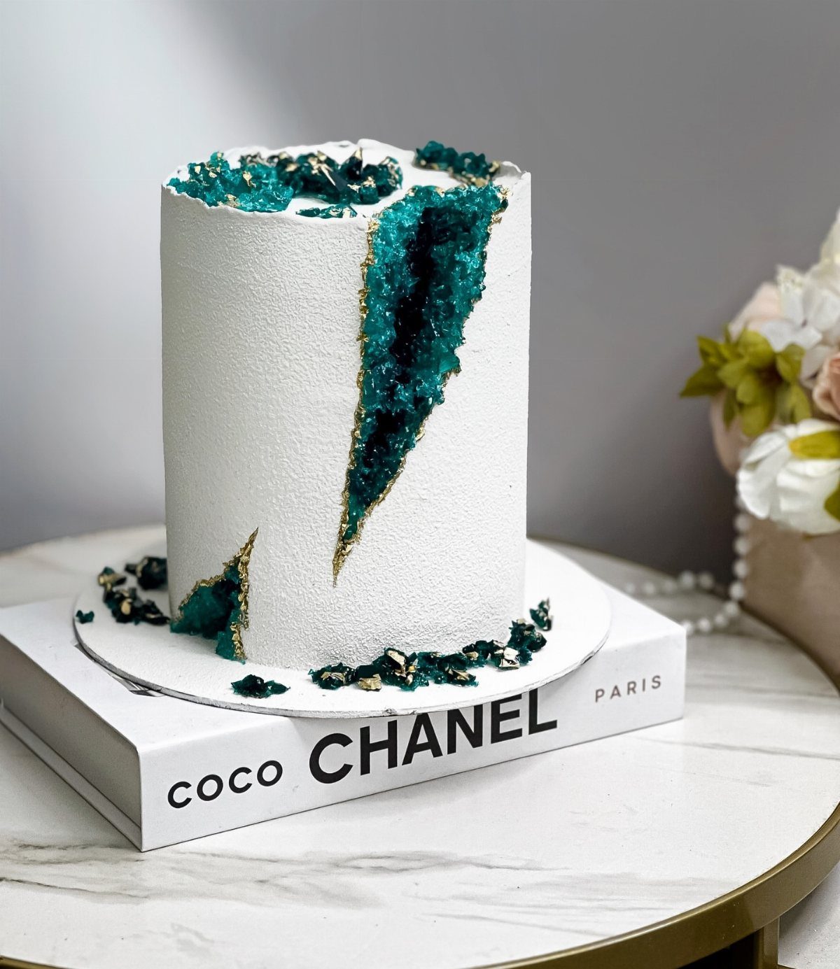 White frosted cake with a teal crystalline geode center and gold edges.