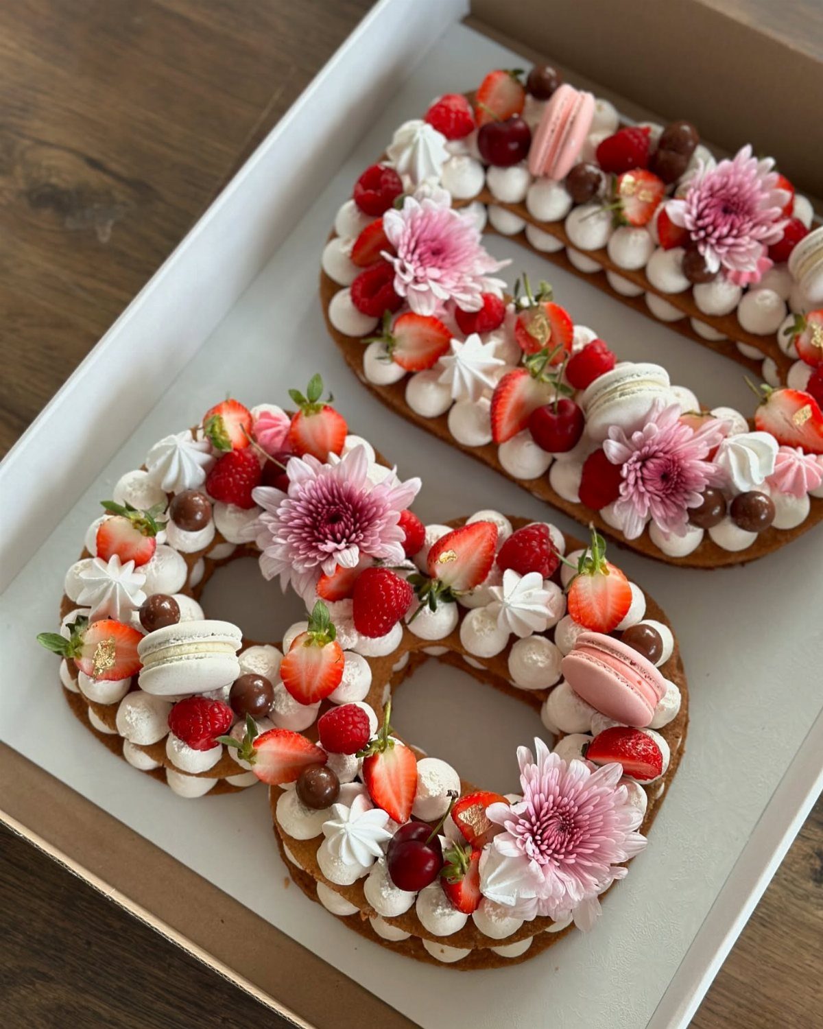 Number 70 cakes decorated with fresh berries, pink macarons, and pink flowers.