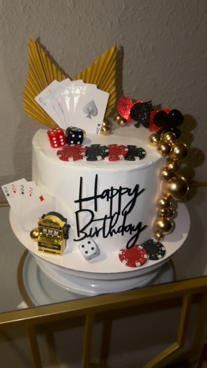 White birthday cake decorated with playing cards, dice, poker chips, and a slot machine.