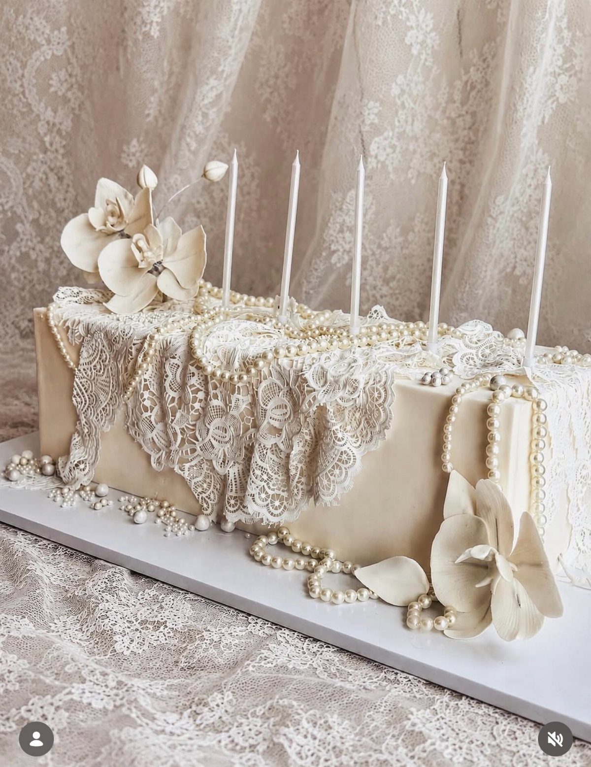 Cream cake decorated with edible white lace, pearls, and white sugar flowers.