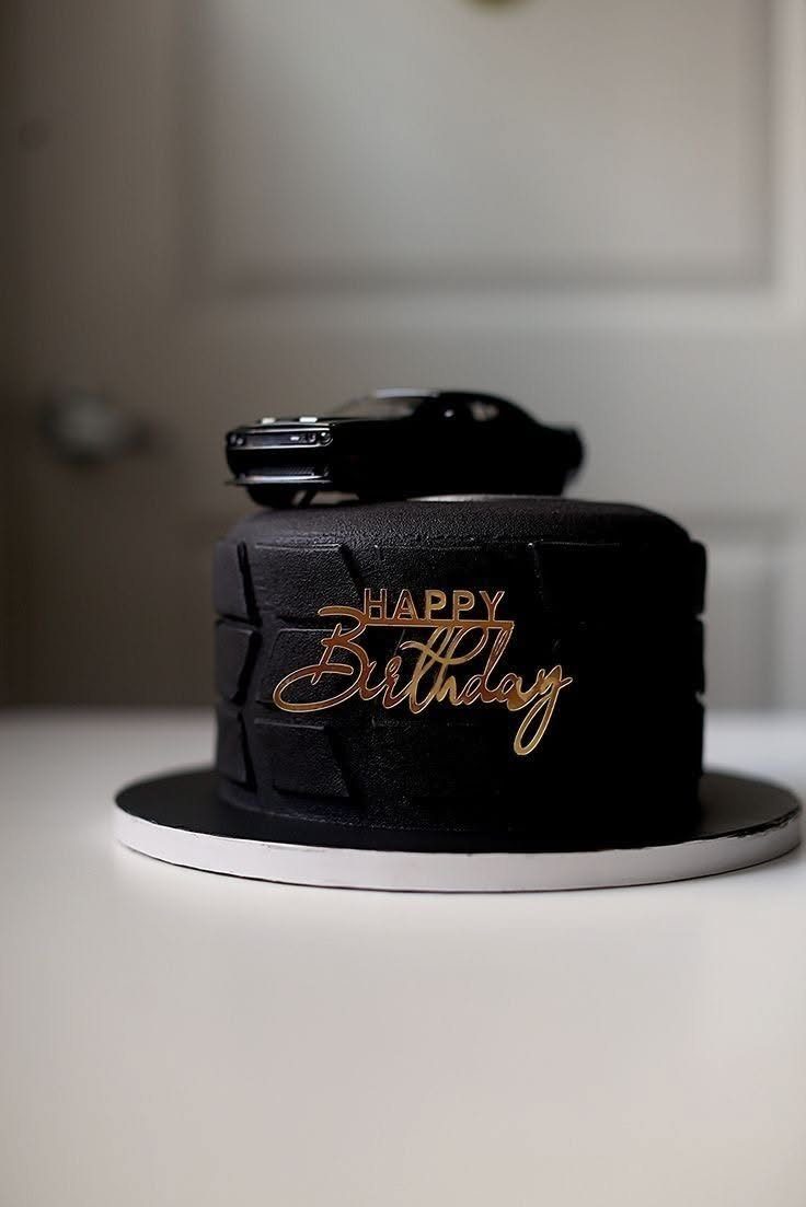 Black frosted birthday cake with gold lettering and a black toy car topper.