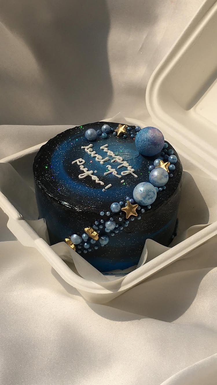 Galaxy cake with dark blue frosting, gold stars, and blue planet decorations.