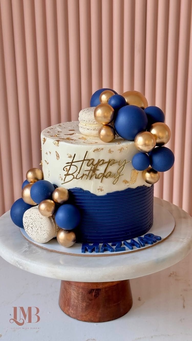 Navy blue and white frosted birthday cake decorated with gold spheres and macarons.