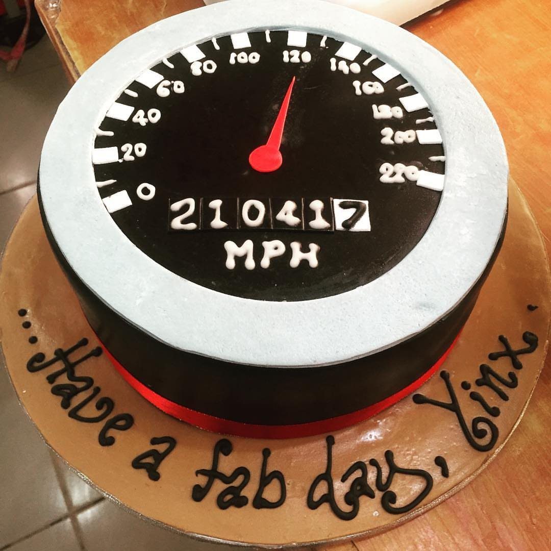 Speedometer cake with a red needle and white numbers on a tan board.