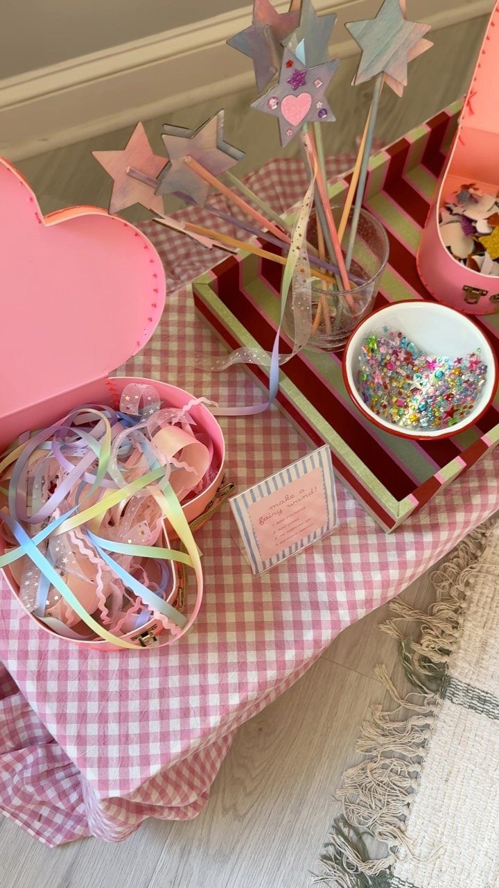 Craft supplies including star wands, colorful ribbons, and sequins on pink checkered fabric.