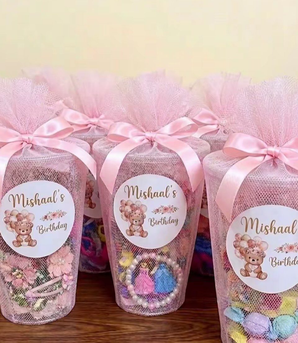 Pink tulle birthday goodie bags filled with treats and personalized teddy bear labels.