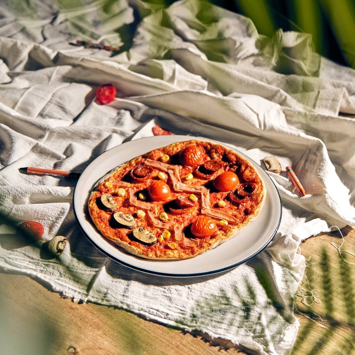 Homemade pizza with cherry tomatoes and mushrooms on a white plate and cloth.