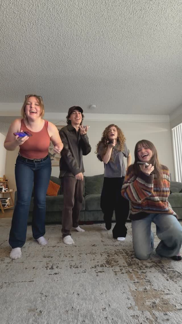 Four young adults singing and dancing with microphones in a cozy living room.