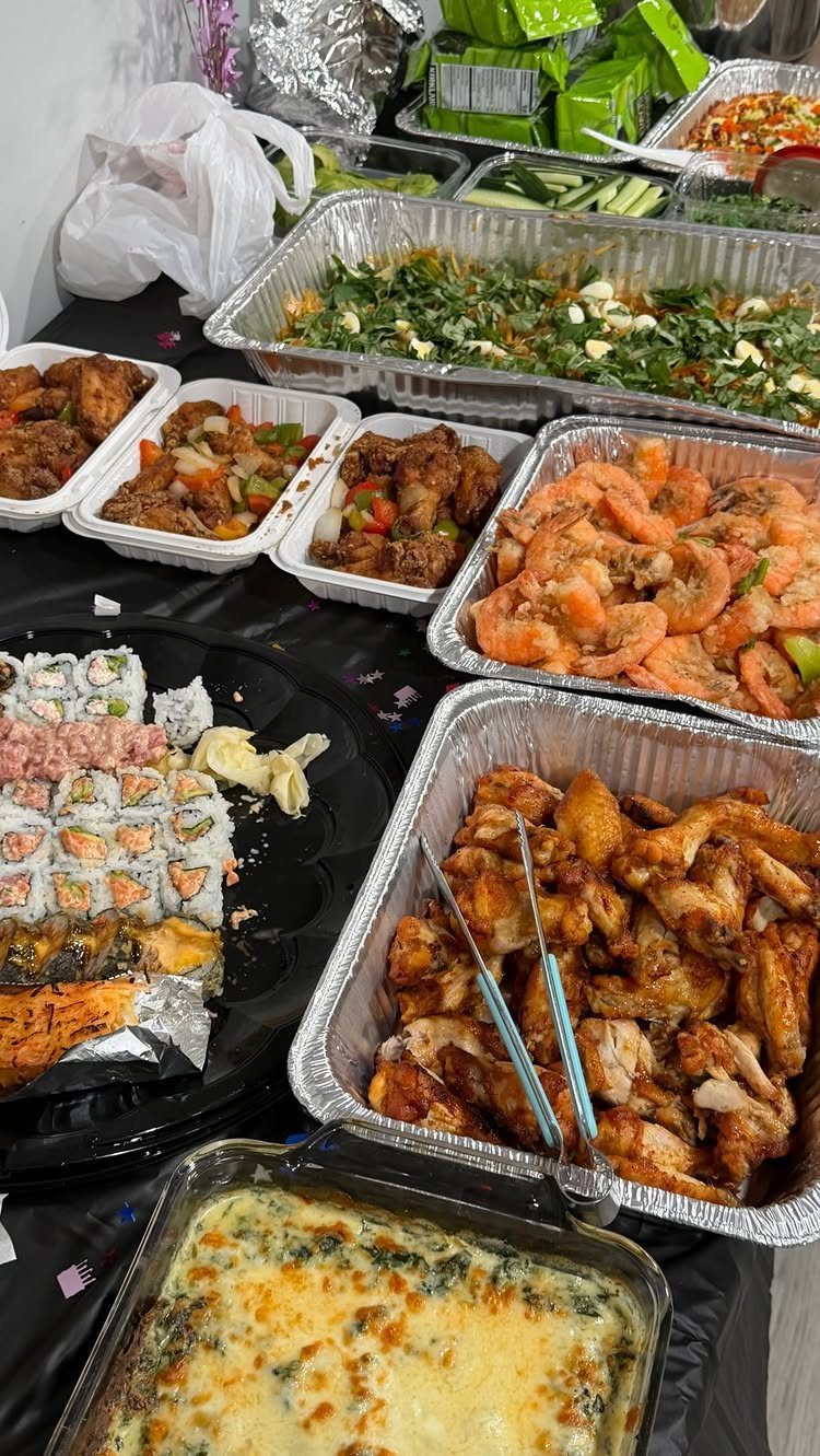 Assorted party foods including sushi, wings, and shrimp in trays on a table.