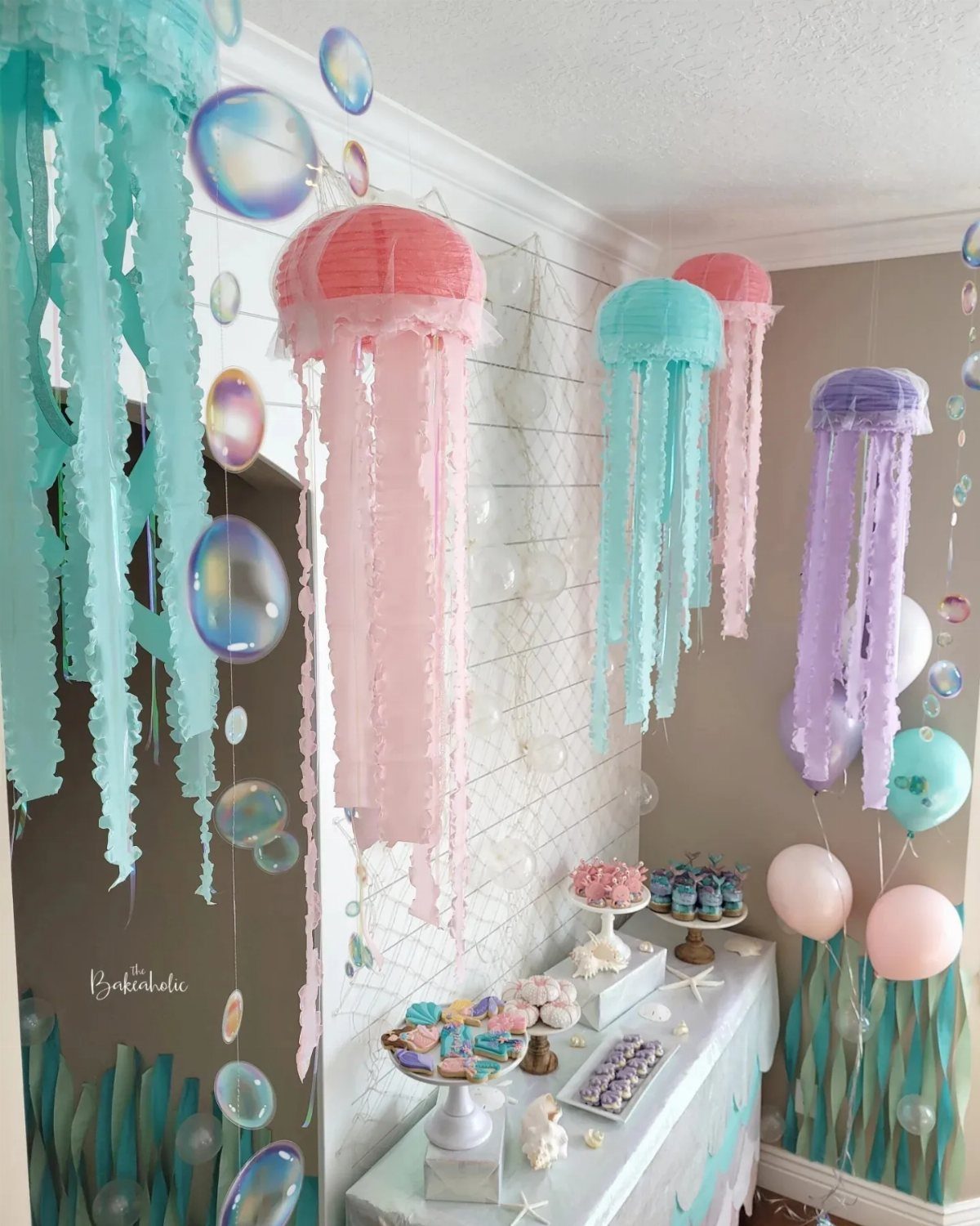 Under the sea party decorations with hanging jellyfish lanterns and a dessert table.