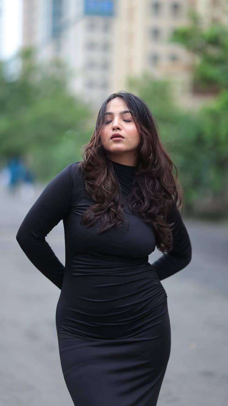 Woman wearing a form-fitting long-sleeved black bodycon dress standing on a city street.