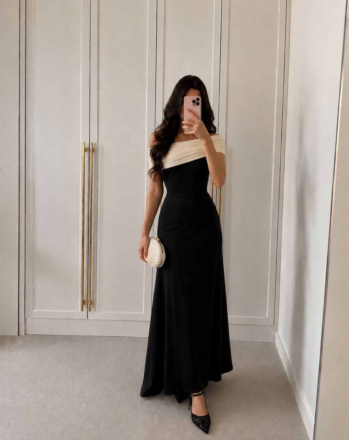 Woman in a long black dress with a white off-the-shoulder neckline and clutch.