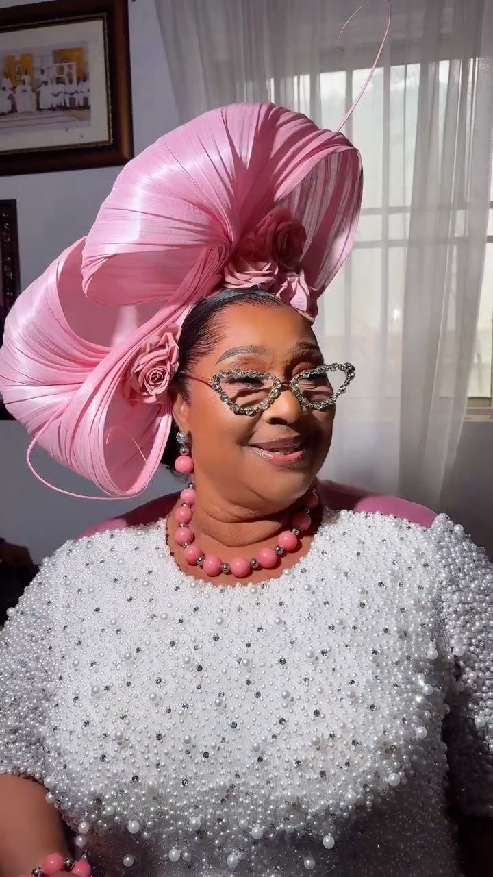 Woman in a pearl-embellished white dress and large pink sculptural fascinator hat.
