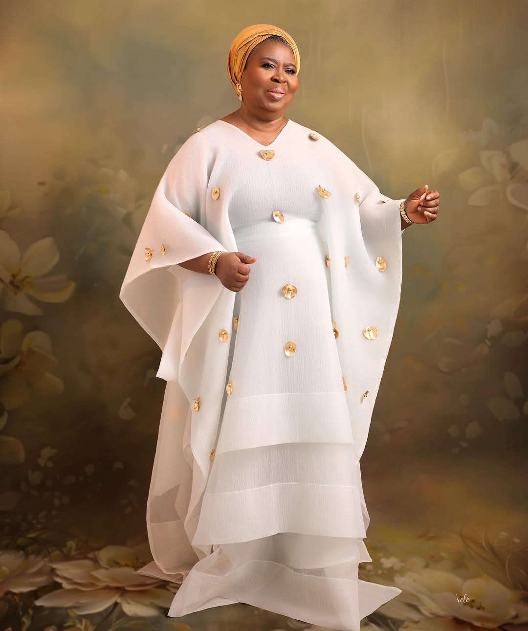 Older woman in a white gown with gold accents and a gold headwrap.