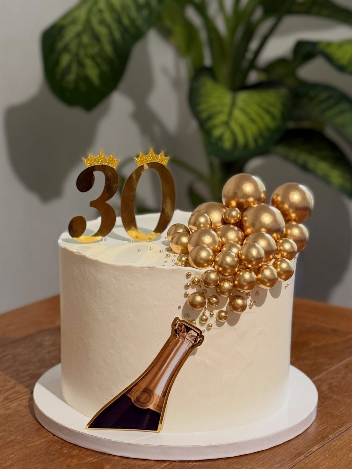 White 30th birthday cake with gold champagne bottle and bubbling gold spheres.