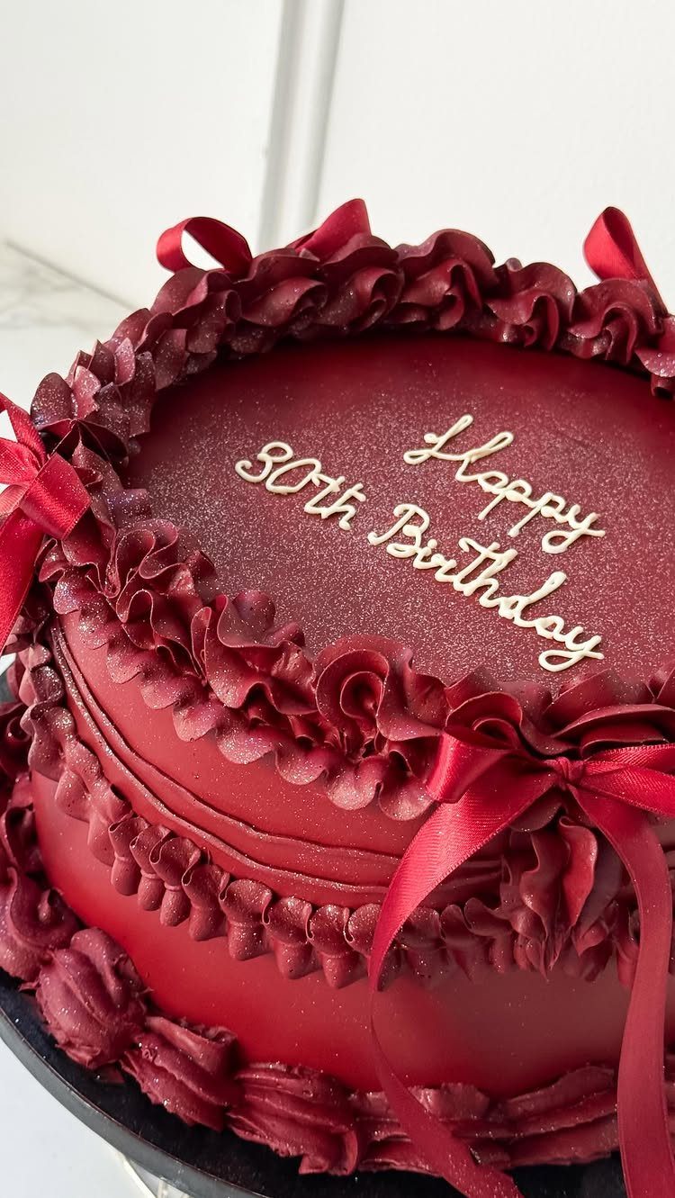 Deep red 30th birthday cake with ruffled frosting and red satin bows.