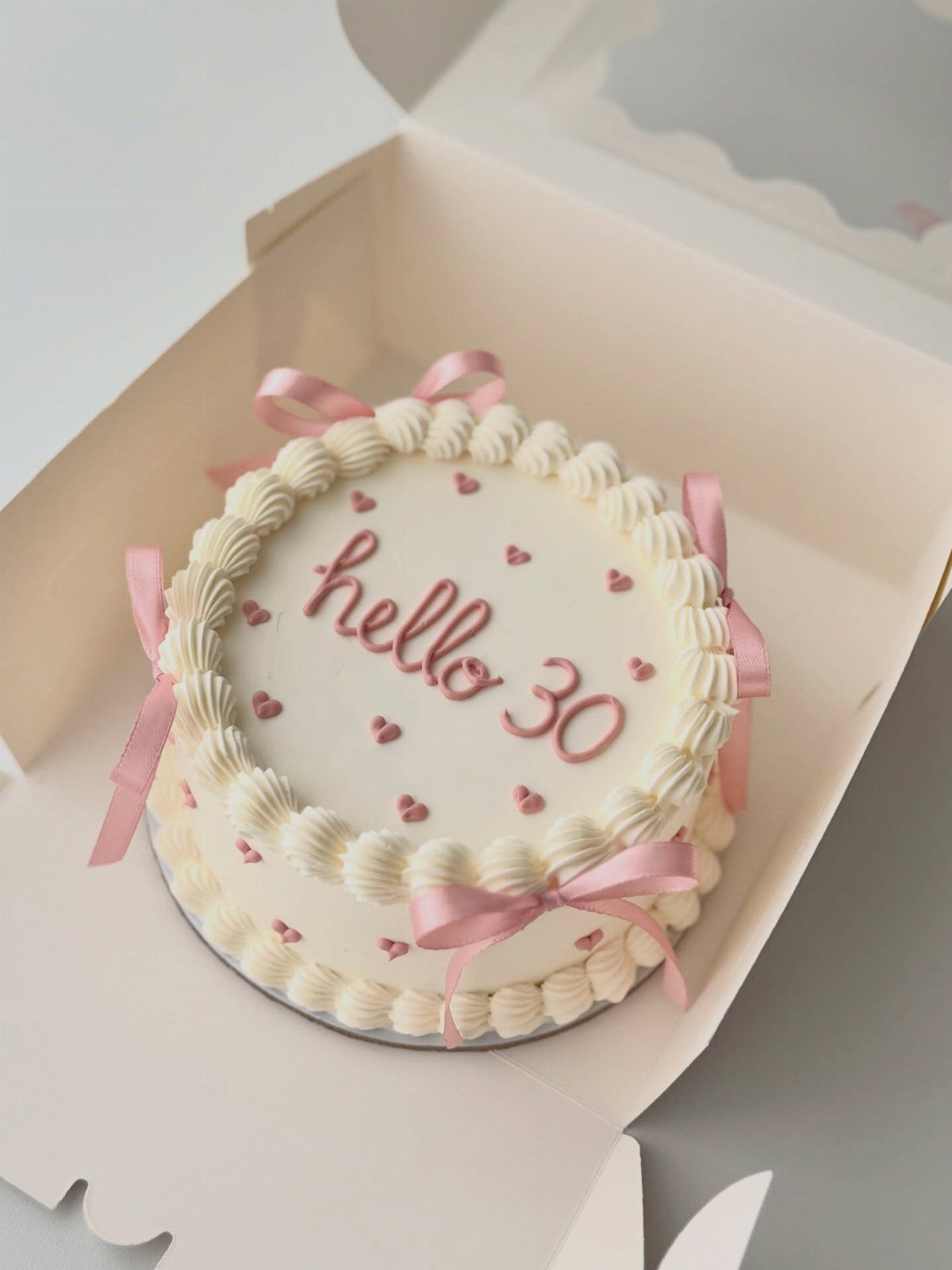 White round birthday cake with pink hearts and ribbons saying hello 30