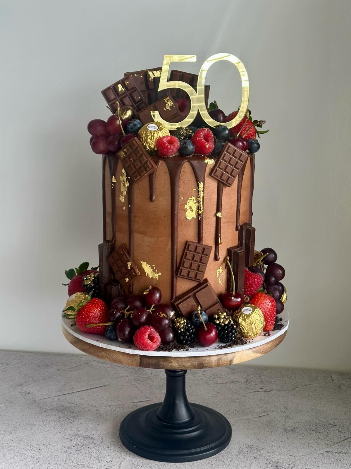Chocolate cake with ganache drip, fresh berries, chocolate bars, and gold 50 topper.