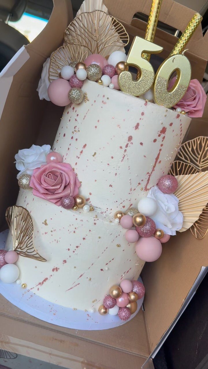 Two-tier cream cake with pink roses, gold accents, and a gold 50 topper.