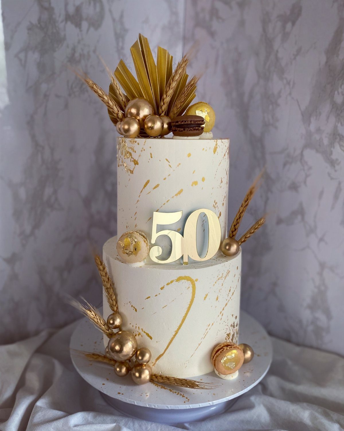 Two-tier white cake with gold leaf, gold spheres, and a gold 50 topper.