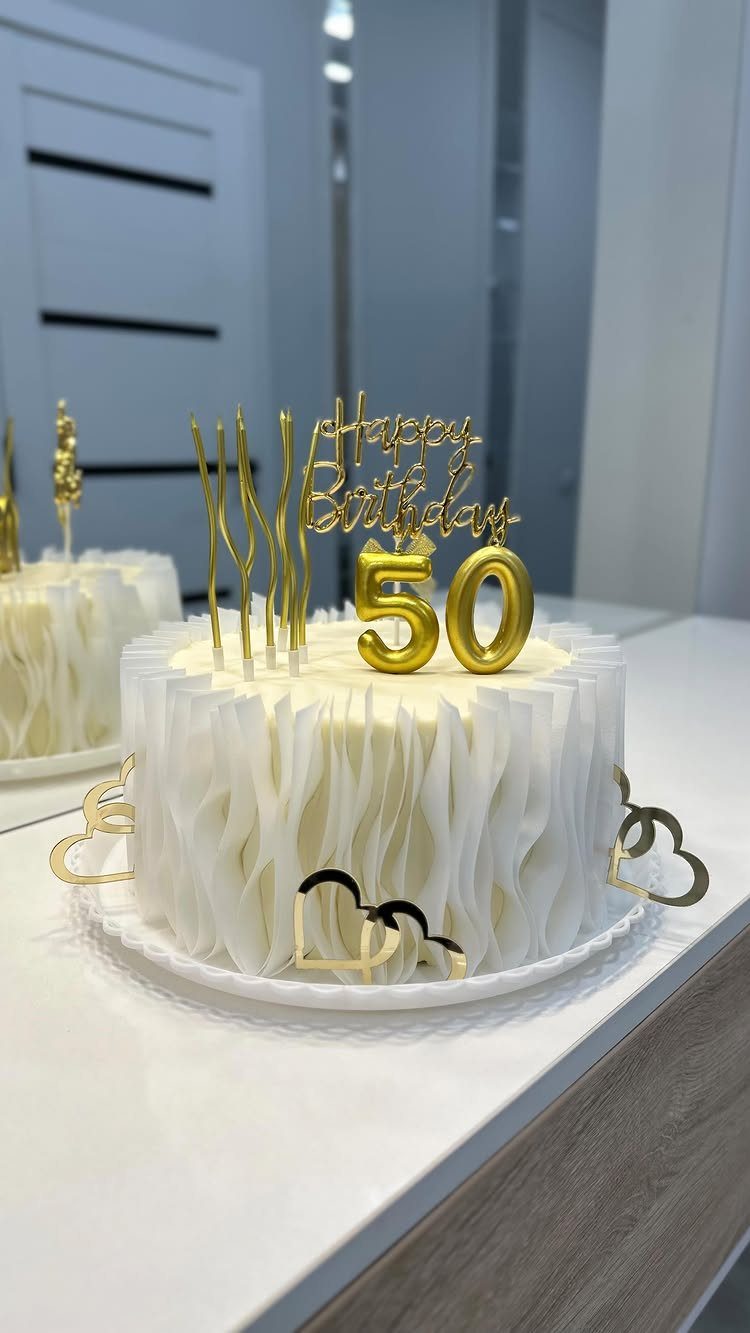 White ruffled birthday cake with gold Happy Birthday 50 topper on white table