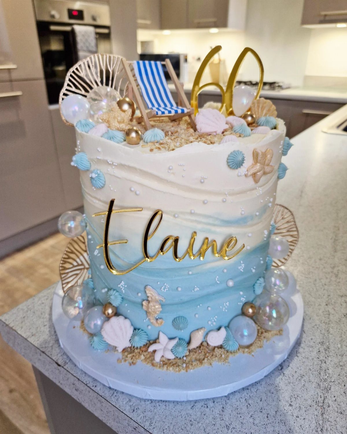 Beach-themed ombré blue cake with seashells, starfish, and a gold 60 topper.