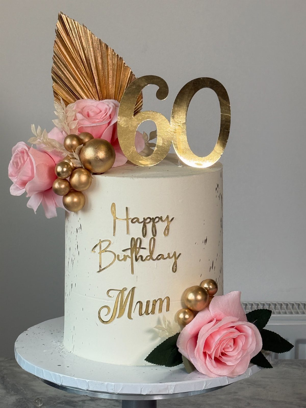 White buttercream cake with gold accents, pink roses, and a gold 60 topper.