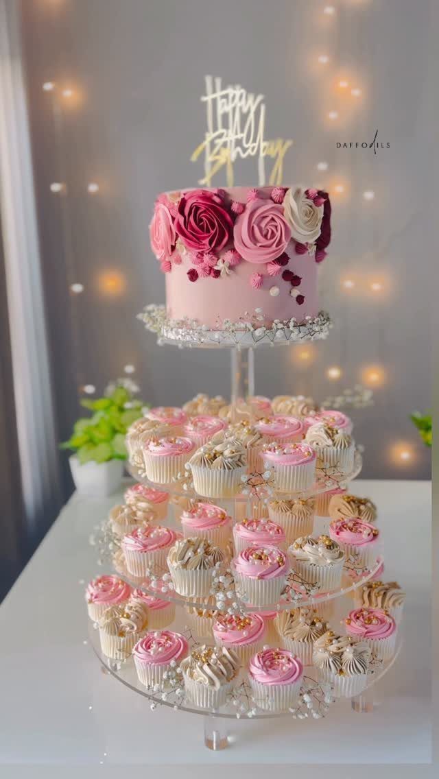 Pink birthday cake with roses atop a tiered stand of pink and white cupcakes