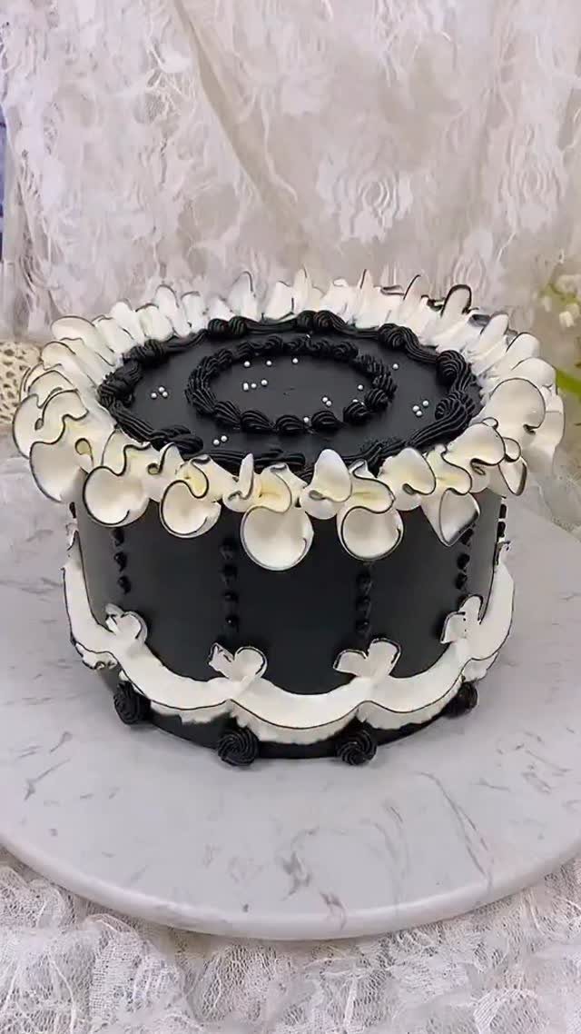 Black round cake with white piped ruffles and silver pearls on marble stand