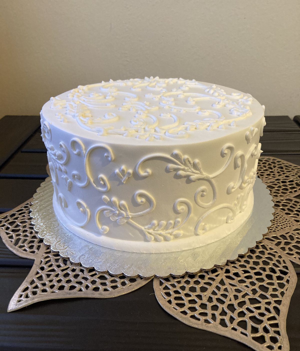 White round cake with intricate piped filigree designs on a gold lace doily