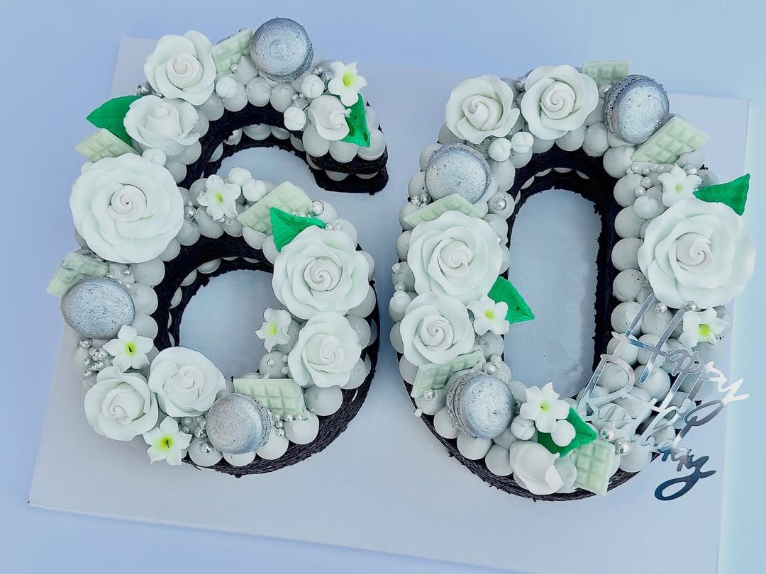 Number 60 cake decorated with white roses, silver macarons, and green leaves