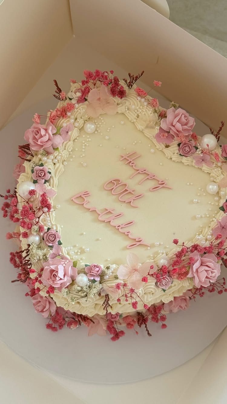 Heart-shaped white birthday cake decorated with pink roses and edible white pearls