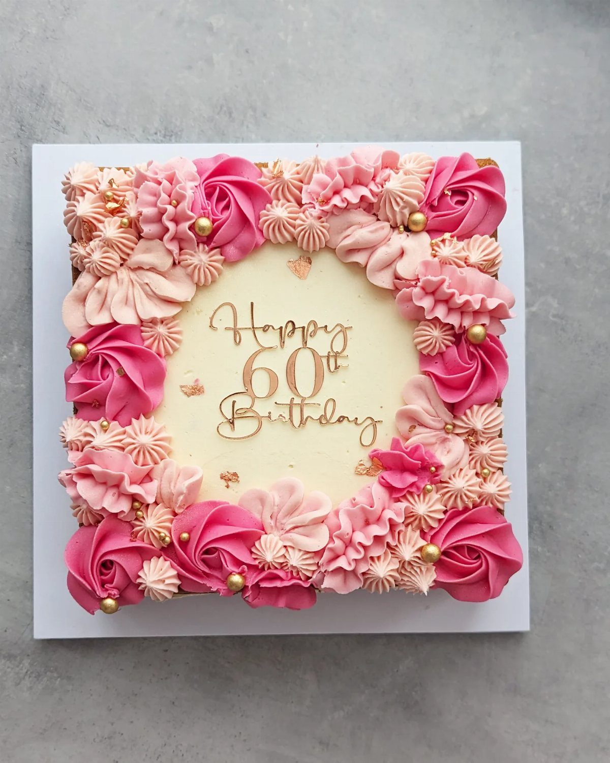 Square white birthday cake decorated with pink buttercream roses and gold 60th topper