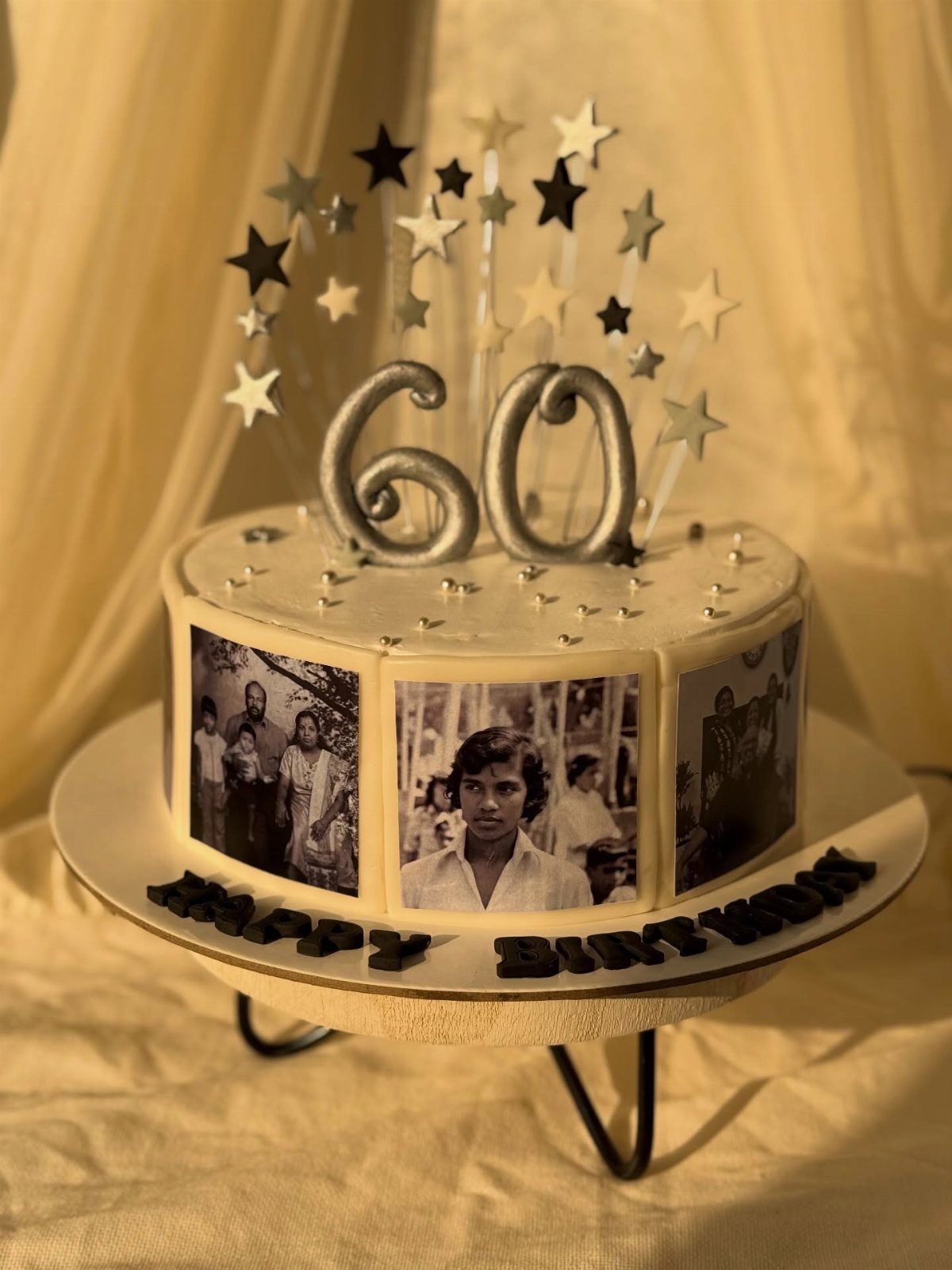 White birthday cake with edible family photos, silver 60 topper, and star decorations.