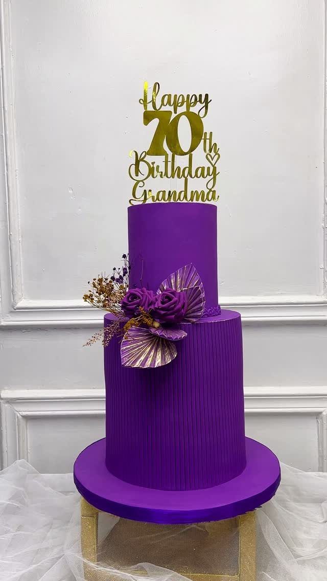 Two-tier purple birthday cake with gold topper and purple floral decorations on gold stand