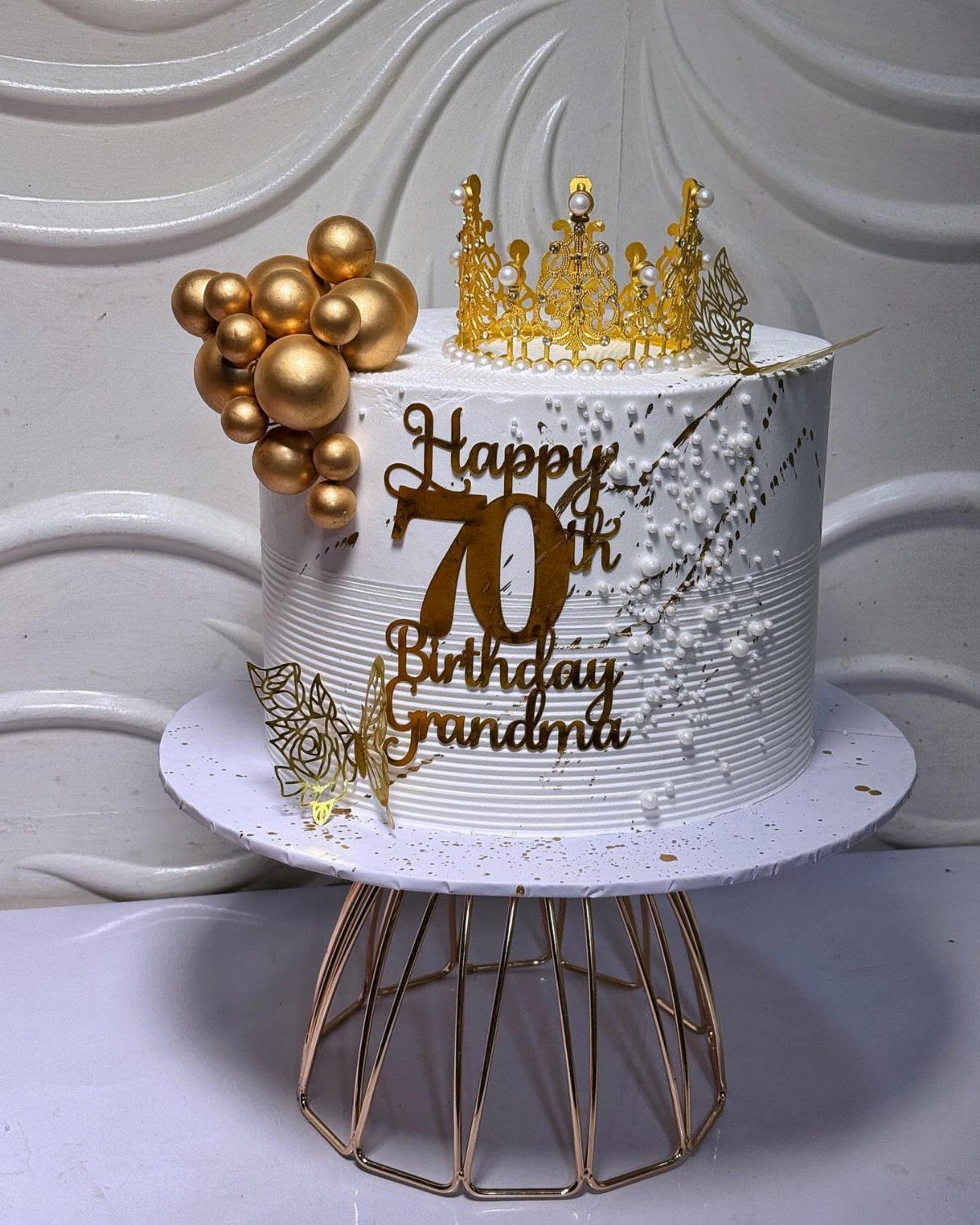 White 70th birthday cake for grandma with gold crown and gold sphere decorations.