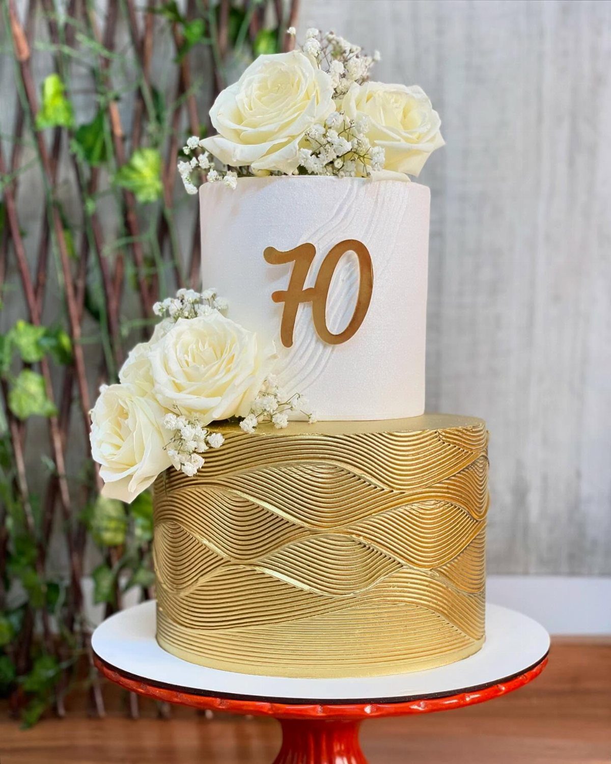 Two-tier gold and white cake with white roses and a gold 70 topper.