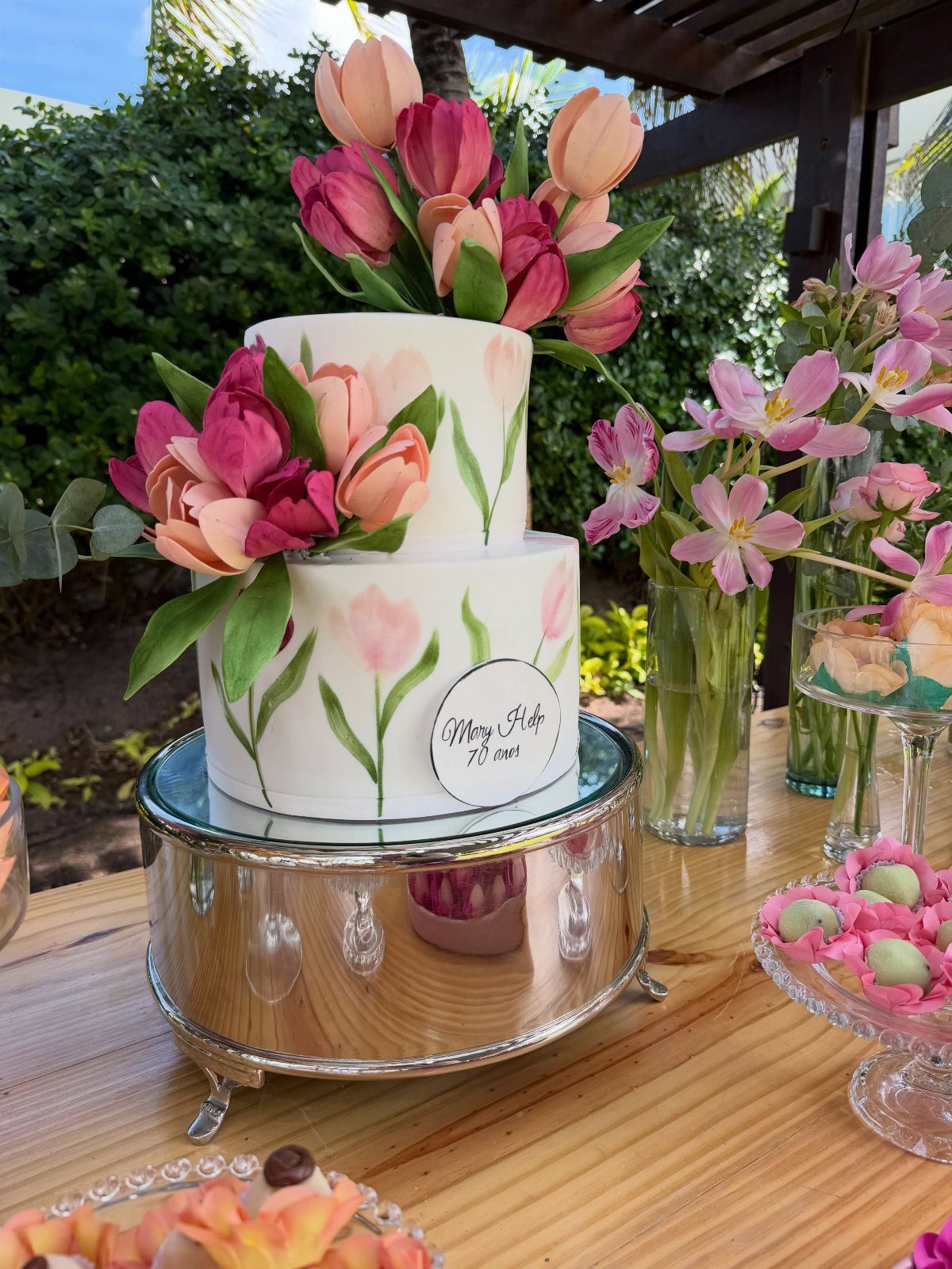 Two-tier white cake with pink tulip decorations on a mirrored silver stand