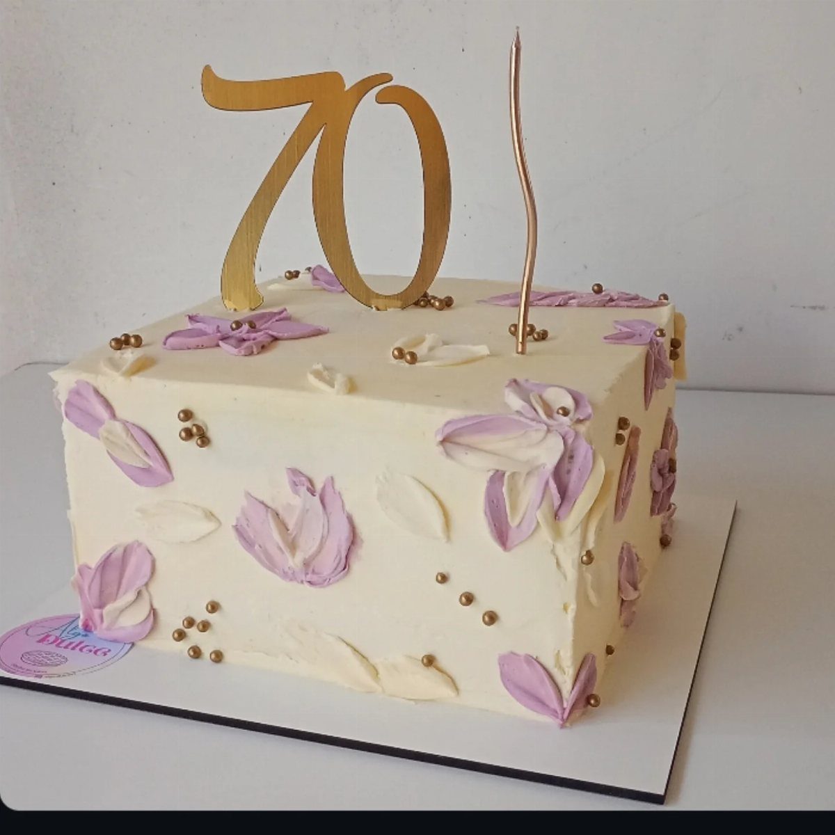 Square white cake with purple floral petals, gold beads, and a gold 70 topper.