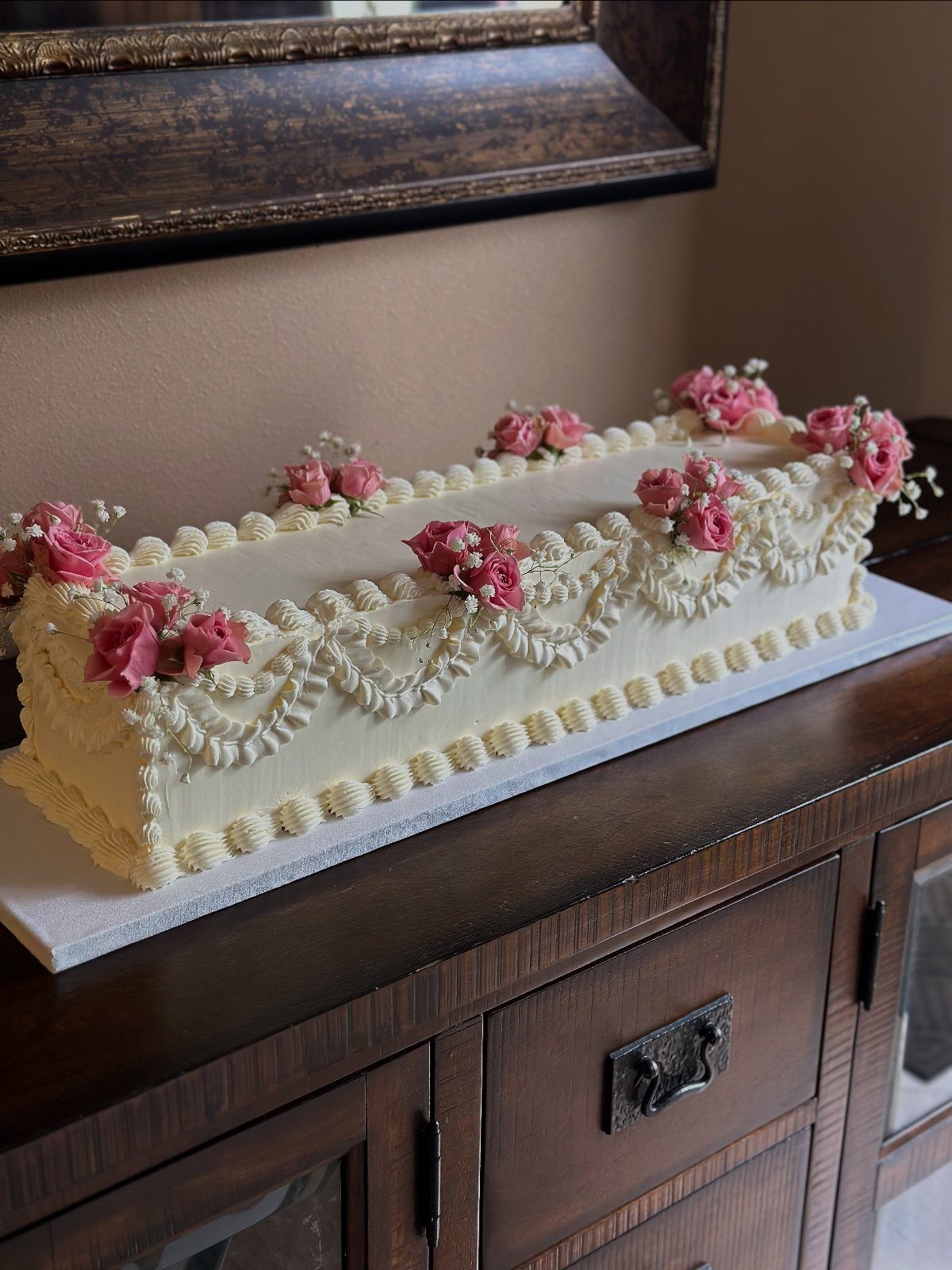 Rectangular white cake with piped lace frosting and small pink rose decorations.