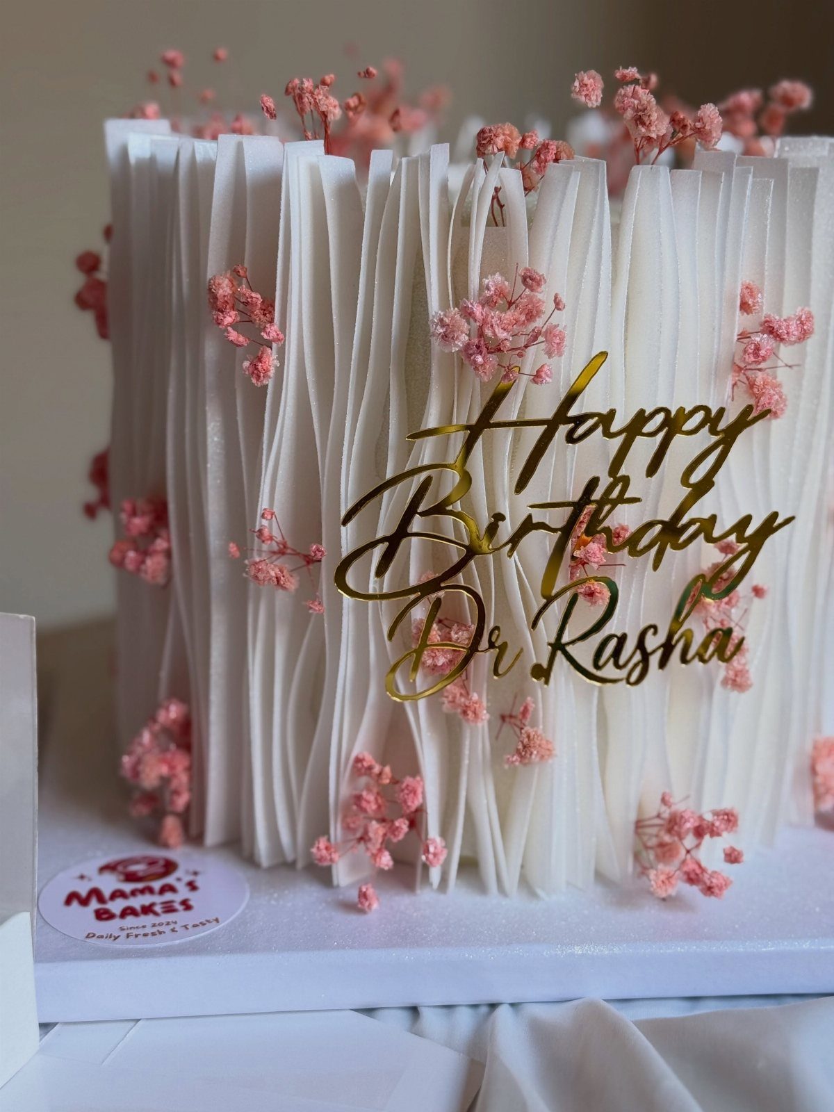 White textured birthday cake with pink flowers and gold Dr Rasha topper