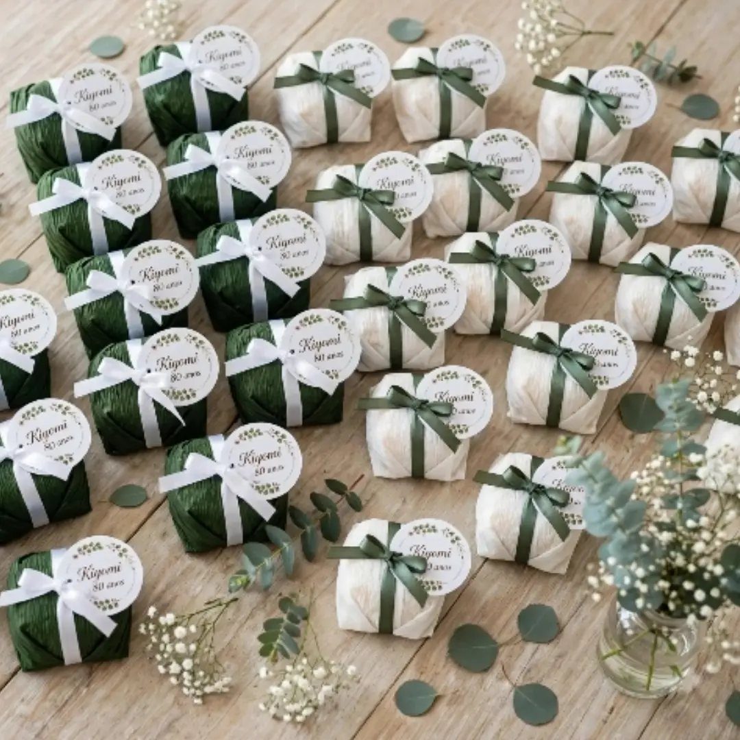Small wrapped gift favors with personalized tags and green ribbons on a wooden table.