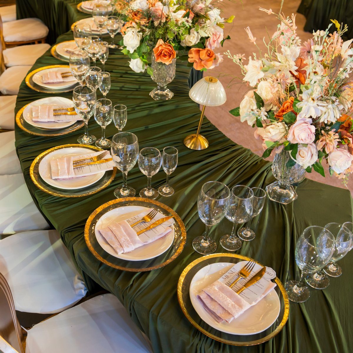 Elegant banquet table with dark green linens, gold-rimmed plates, and orange floral centerpieces.
