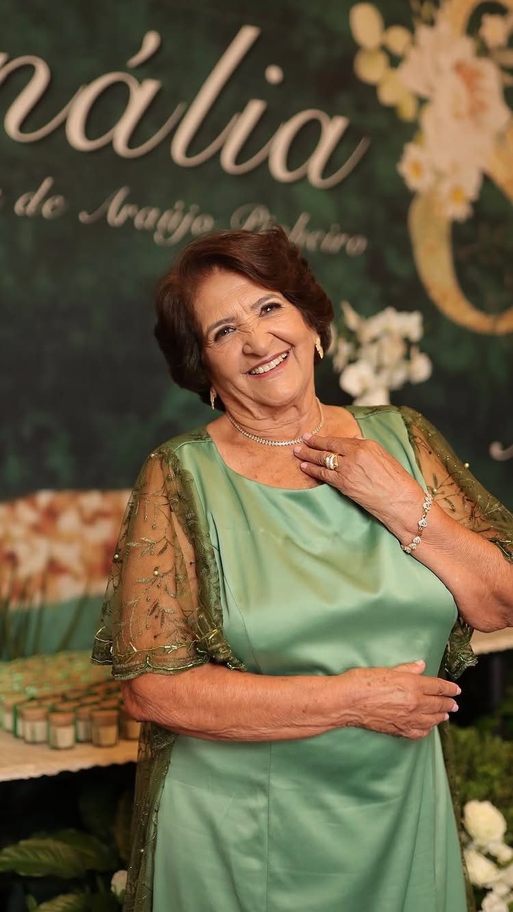 Smiling older woman in a sage green satin dress at an elegant celebration.