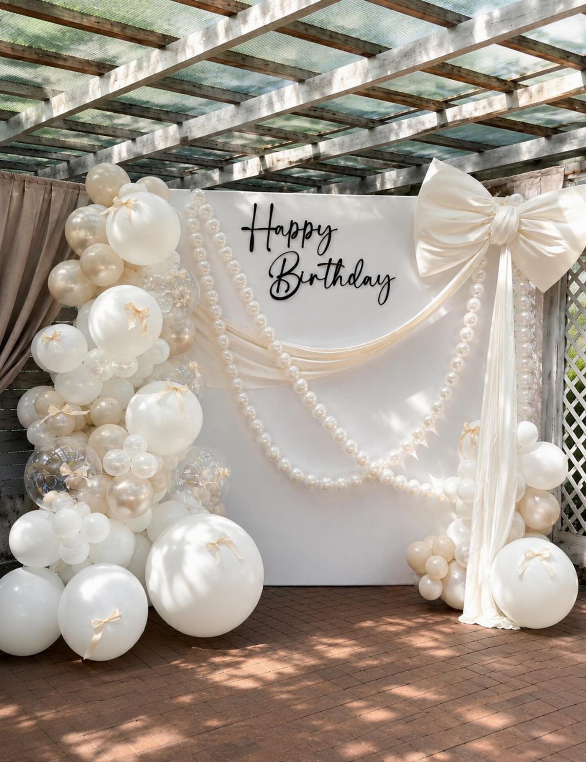 White birthday backdrop with balloons, draped fabric, and a large white bow.