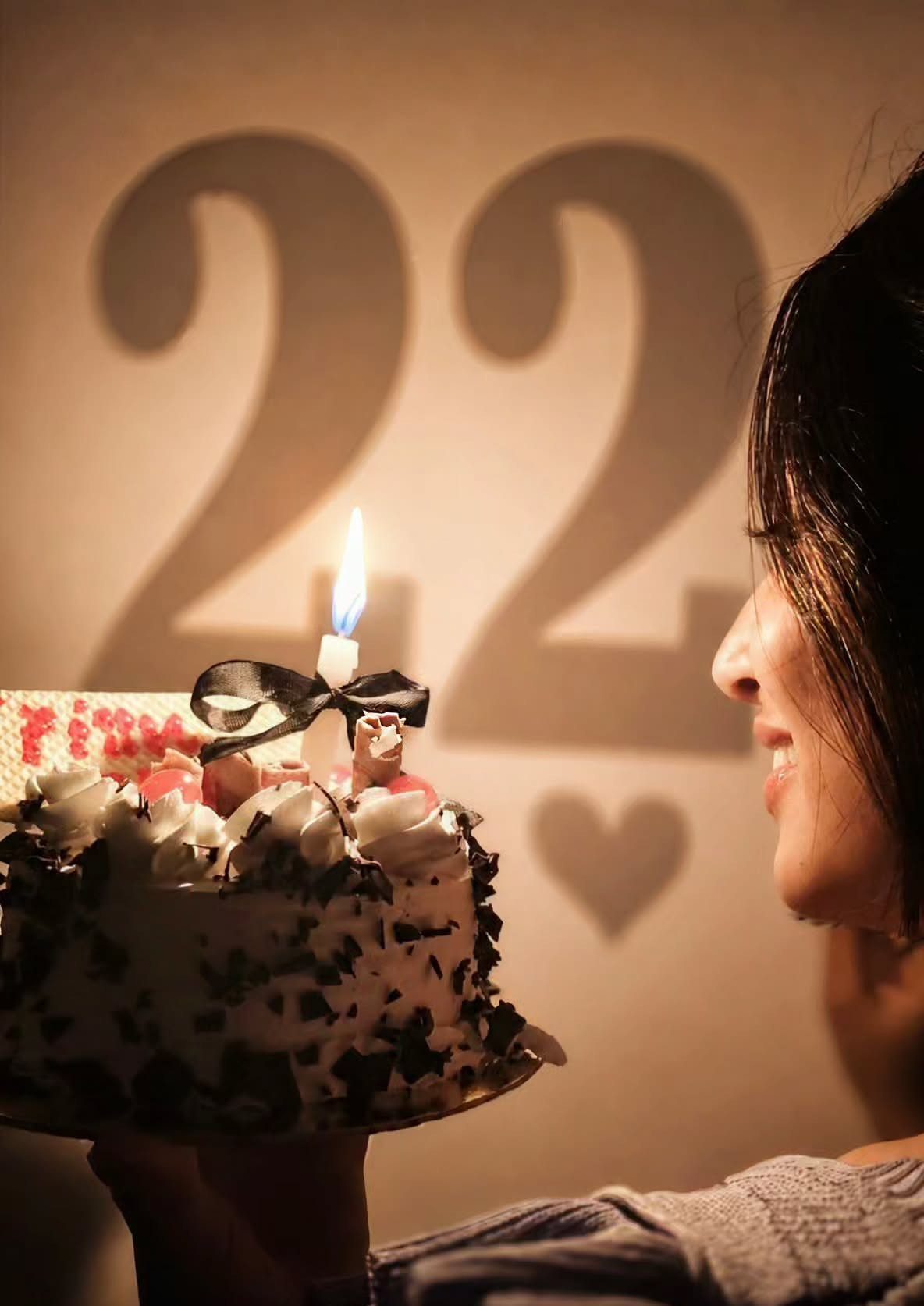 Woman holding a birthday cake with a shadow of number 22 on wall
